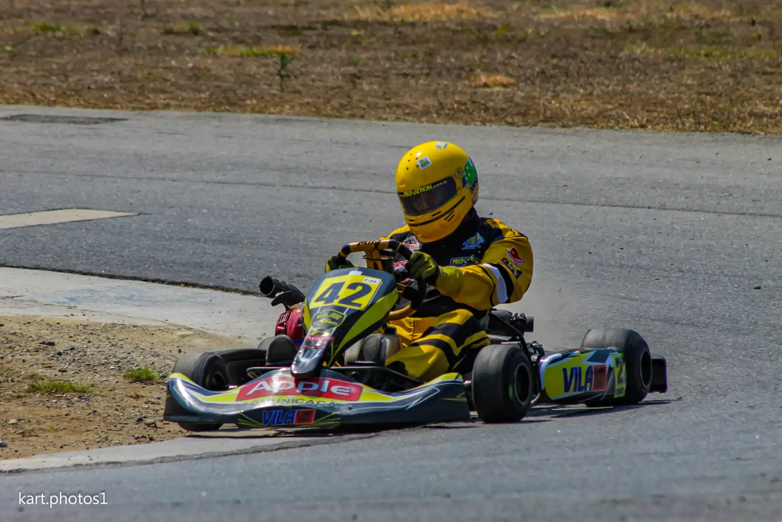 Piloto de kart executando a tangência perfeita na curva com o volante reto, ilustrando o traçado esportivo e a técnica de entrar devagar para sair rápido